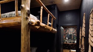 Una cama litera de diseño rústico, un sofá de color oscuro y un suelo de madera.