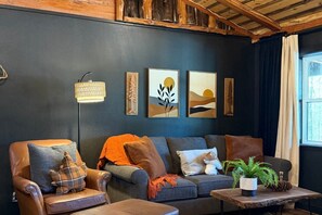 Un salón acogedor con una pared azul oscuro, un sofá de cuero, una mesa de centro de madera y una lámpara de pie.