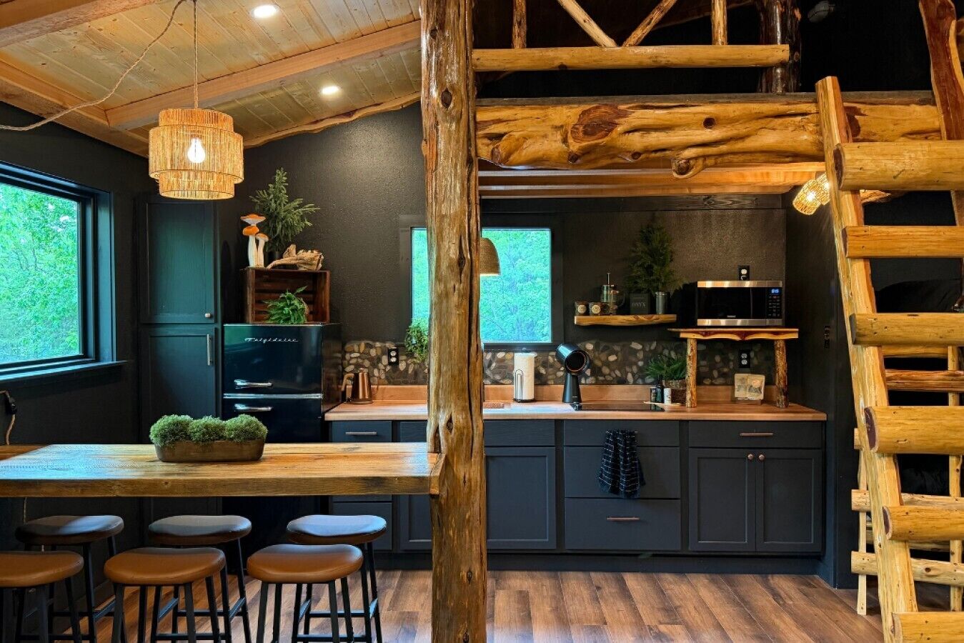 A rustic kitchen with a wooden ceiling, a built-in stove, and a wooden ladder.
