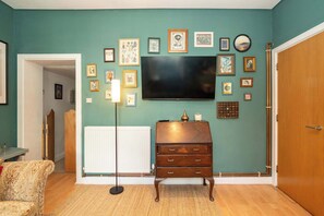 Ein Wohnzimmer mit türkisfarbenen Wänden, einem flachbildfernseher, der über einer Holzkommode angebracht ist, und verschiedenen gerahmten Bildern an der Wand.