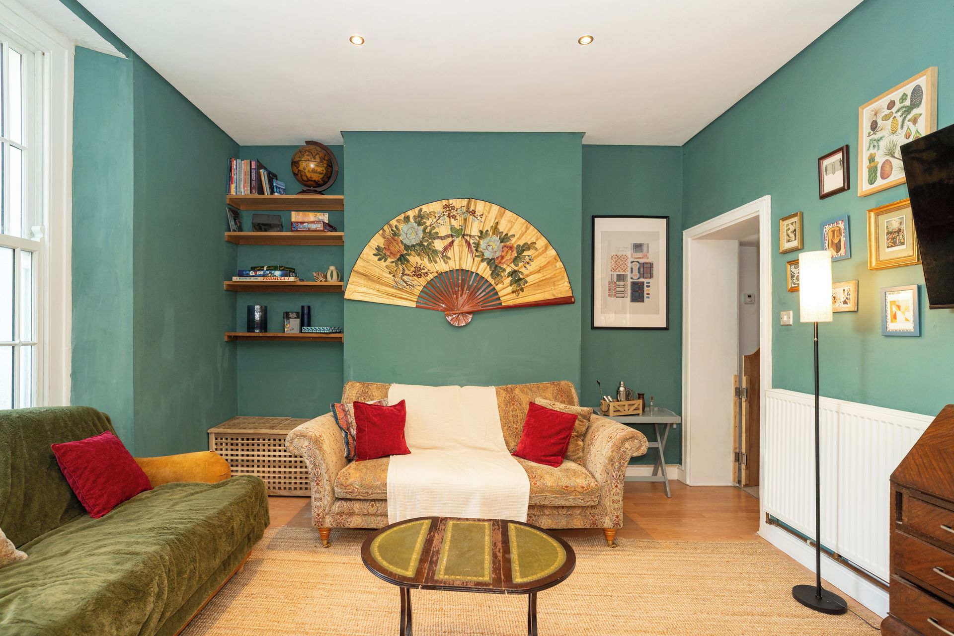 A living room with a sofa, a coffee table, a bookshelf, a fan, and a framed picture on the wall.