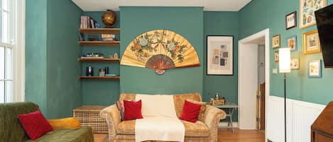 A living room with a sofa, a coffee table, a bookshelf, a fan, and a framed picture on the wall.