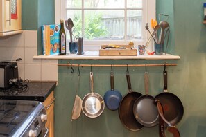 A kitchen with a window, a shelf with books and kitchen utensils, and hanging pots. - 1BDR 1BA Flat on Vibrant Gloucester Road (Bristol City)