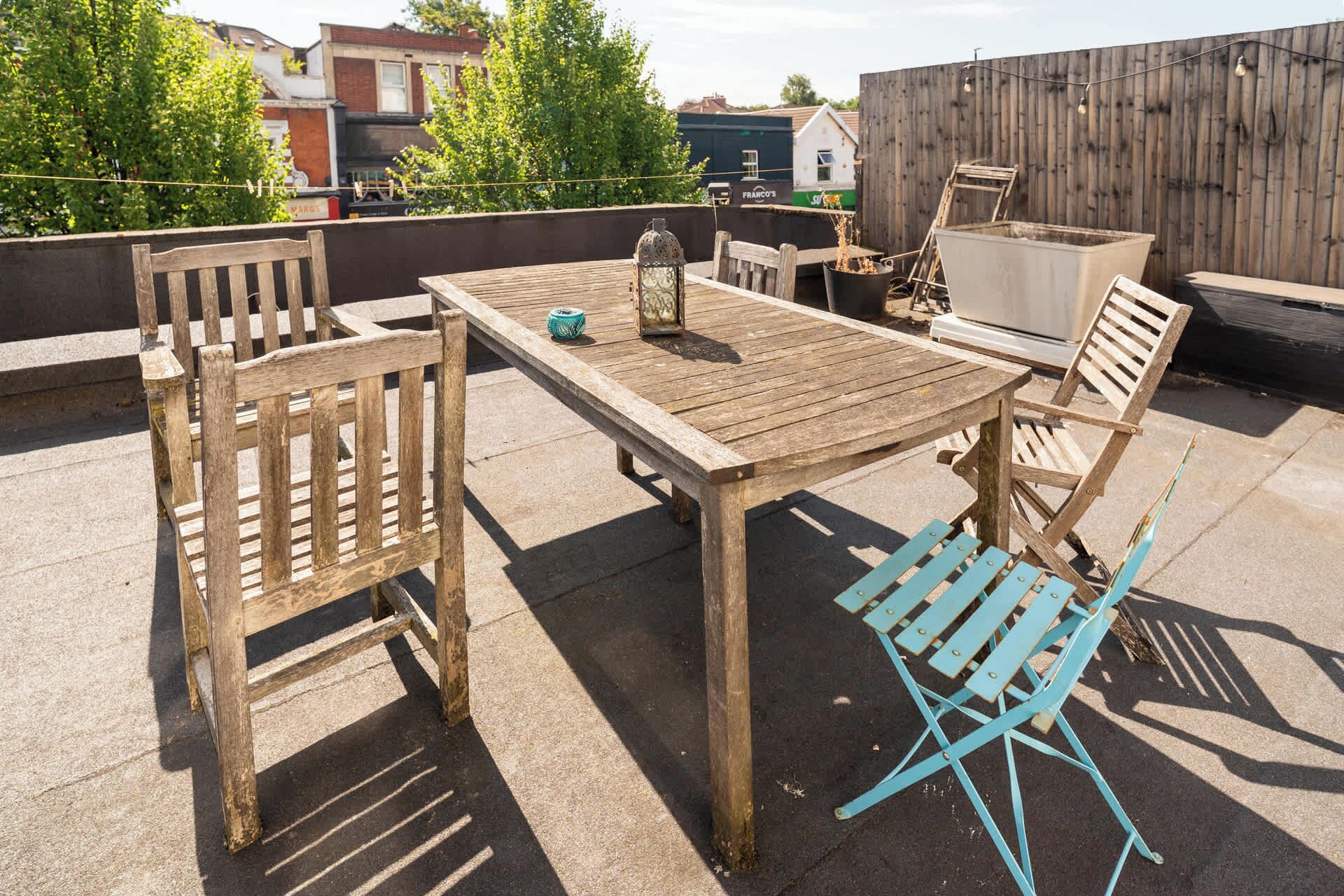 An outdoor patio with a wooden table and chairs, a lantern, and a trash bin.