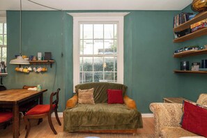 Ein gemütliches Wohnzimmer mit einem grünen Sofa, einem Holzesstisch und einem Fenster mit Blick auf Grünflächen.
