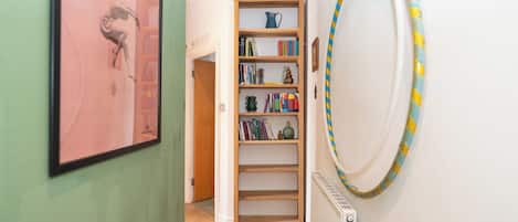A hallway with a bookshelf, a radiator, and a framed picture on the wall.