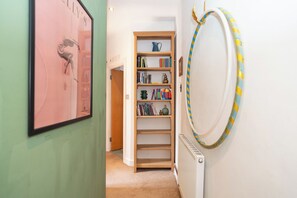 Een gang met een boekenplank, een radiator en een ingelijst schilderij aan de muur.
