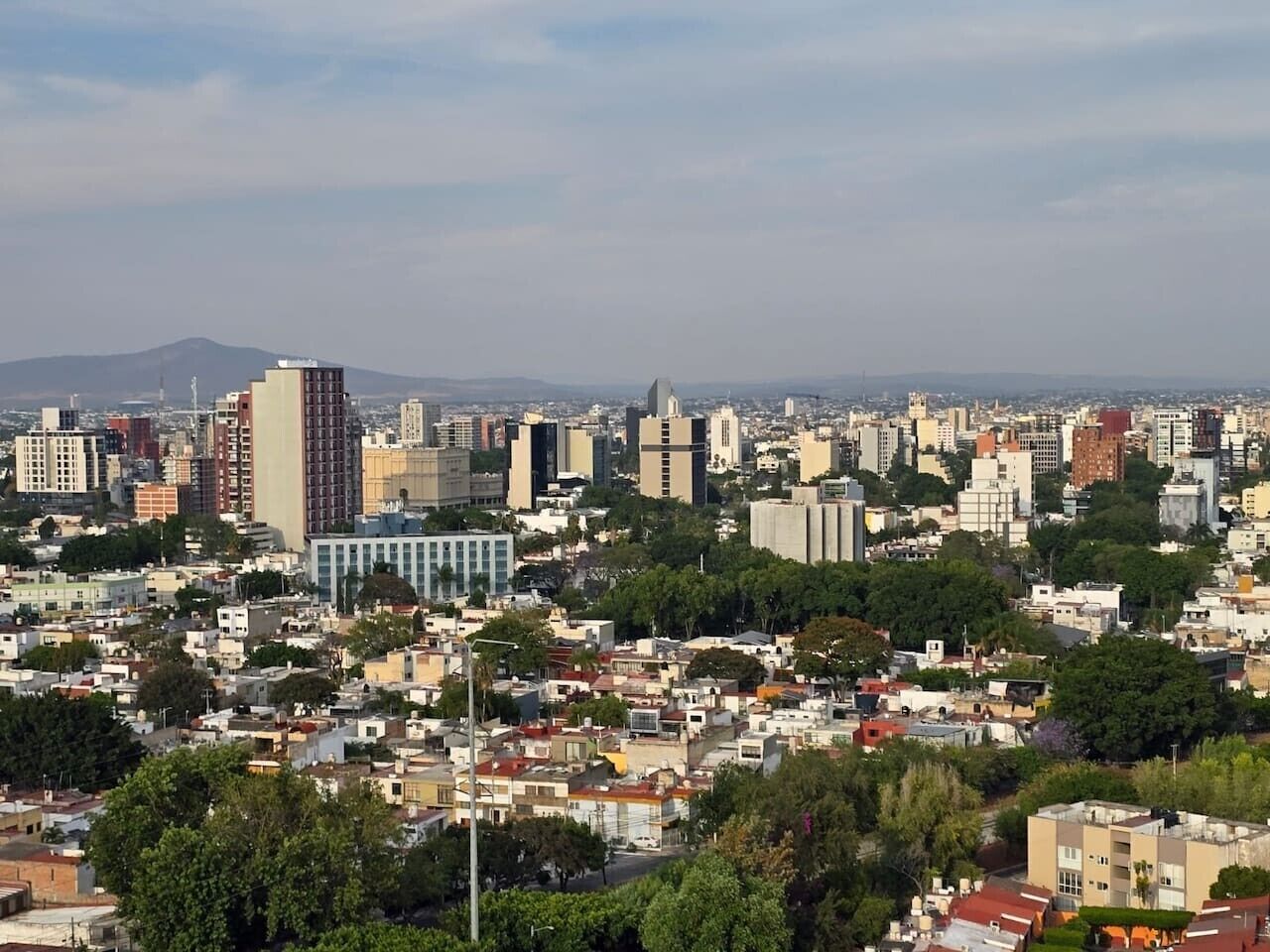 A cityscape with a mix of high-rise and low-rise buildings, a clear sky, and distant mountains.
