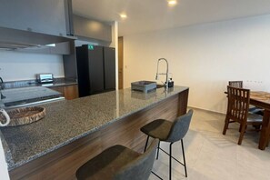 A modern kitchen with a granite countertop, stainless steel appliances, and a dining area with a wooden table and chairs. - Departamento Nhaos Minerva (Guadalajara)