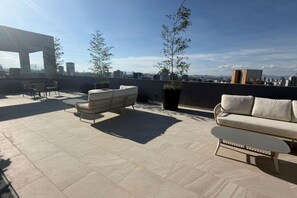 Terraço no telhado com móveis de exterior, incluindo um sofá e cadeiras, e uma planta em vaso.
