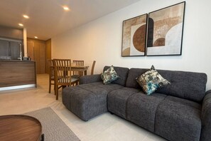 Ein modernes Wohnzimmer mit grauem Sofa, zwei passende Kissen, einem Holzessttisch mit Stühlen und einer Küchenzeile im Hintergrund.