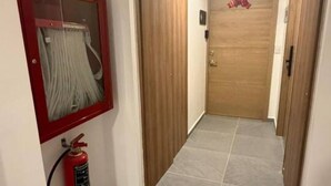 A hallway with a fire extinguisher mounted on the wall, a fire hose reel, and a wooden door at the end. - Departamento Nhaos Minerva (Guadalajara)