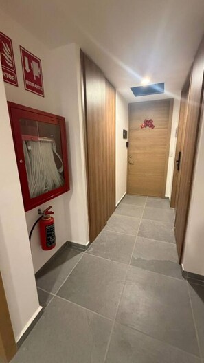 A hallway with a fire extinguisher mounted on the wall, a fire hose reel, and a wooden door at the end. - Departamento Nhaos Minerva (Guadalajara)