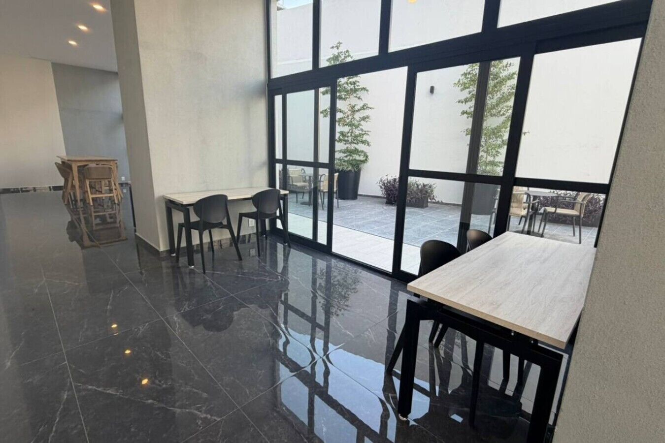 A modern interior with a polished floor, large windows, and a seating area with tables and chairs.