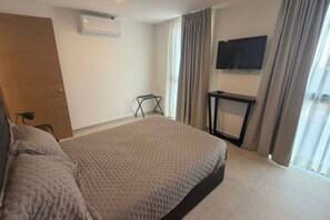 A hotel room with a bed, a TV mounted on the wall, a window with curtains, and a small table. - Departamento Nhaos Minerva (Guadalajara)
