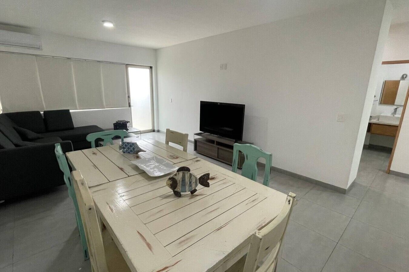 A living room with a sofa, a dining table, a television, and a kitchen area.