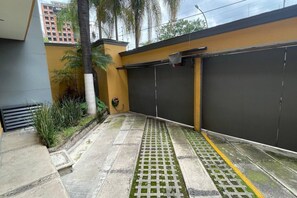 A courtyard with a paved walkway, a gated entrance, and a building with a yellow facade. - Departamento Minerva (Guadalajara)