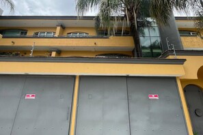 Ein Gebäude mit gelber Fassade, zwei graue Garagentore mit der Aufschrift 'KEIN PARKEN' und eine Palme.