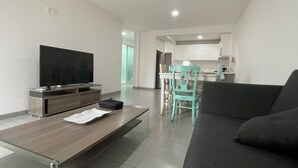 Ein modernes Wohnzimmer mit Flachbildfernseher, Couchtisch aus Holz, einem blaugrünen Sessel und einem dunklen Sofa.