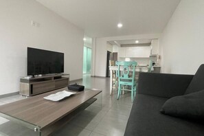 A modern living room with a flat-screen TV, a wooden coffee table, a teal chair, and a dark sofa. - Departamento Minerva (Guadalajara)