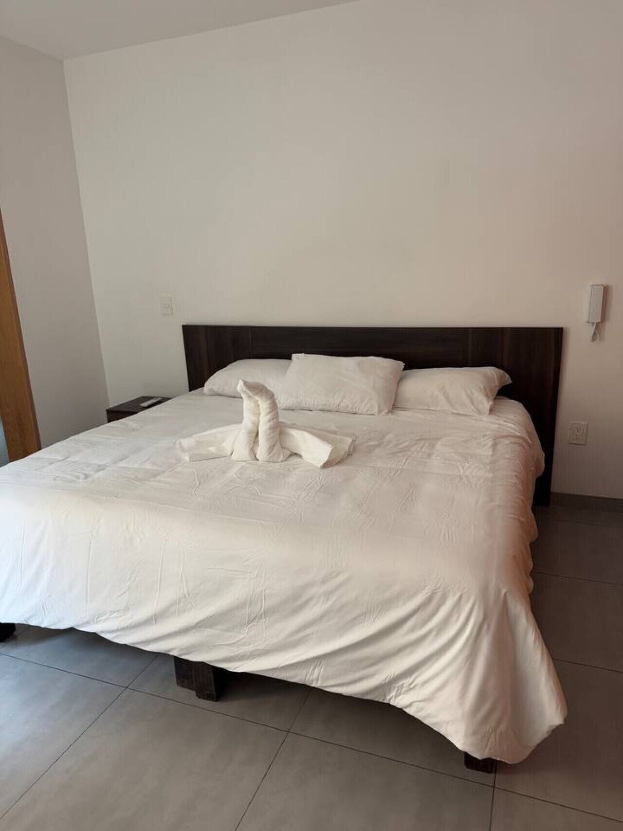A neatly made bed with a dark headboard, white linens, and a towel arranged on the bed.