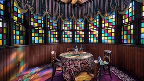 A room with a round table, chairs, and colorful stained glass windows.