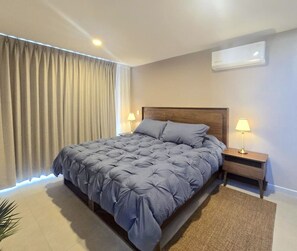 A hotel room with a large bed, a nightstand with a lamp, an air conditioning unit, and a window with curtains. - Departamento NHAOS Minerva (Guadalajara)