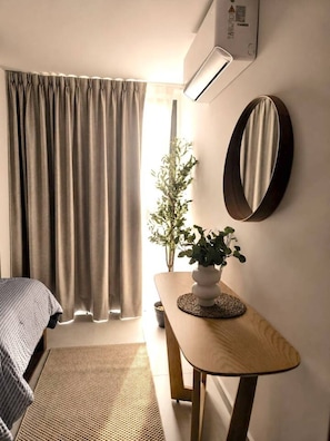 Ein Zimmer mit einem Bett, einem kleinen Tisch mit einer Pflanze, einem Spiegel und einer Klimaanlage.