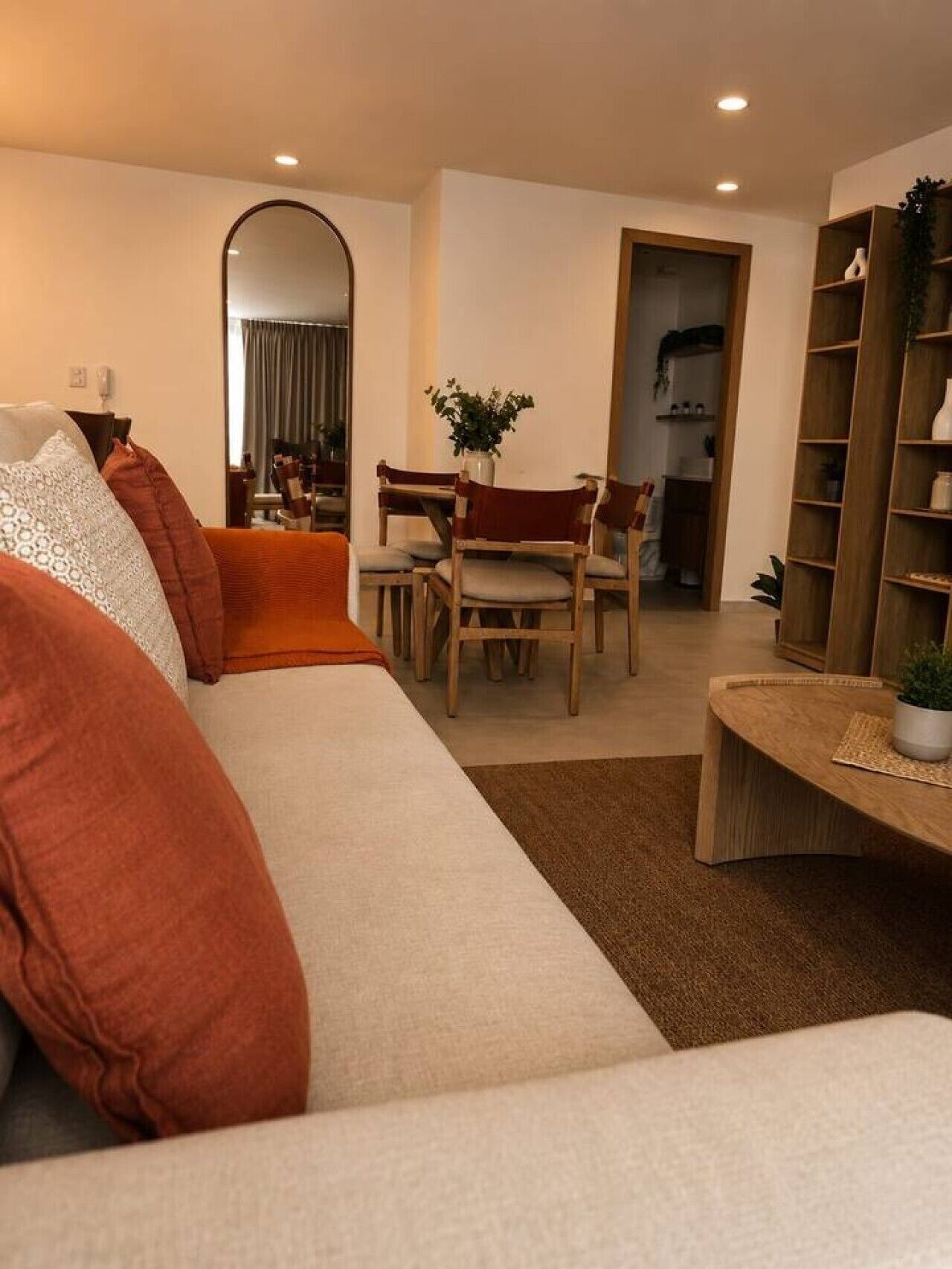 A living room with a sofa, a dining table with chairs, a bookshelf, and a mirror.