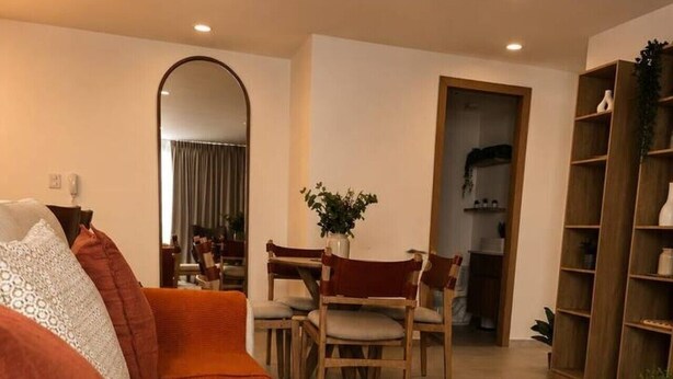 A living room with a sofa, a dining table with chairs, a bookshelf, and a mirror. - Departamento NHAOS Minerva (Guadalajara)