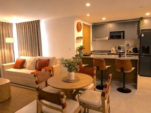 A modern living room with a sofa, a dining table with chairs, a kitchen area with a microwave, and a bar stool. - Departamento NHAOS Minerva (Guadalajara)