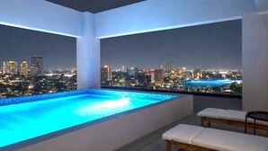 A rooftop infinity pool with a cityscape view at night. - Departamento NHAOS Minerva (Guadalajara)