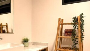 A bathroom with a wooden vanity, a mirror, a sink, and a wooden shelf with plants. - Departamento NHAOS Minerva (Guadalajara)