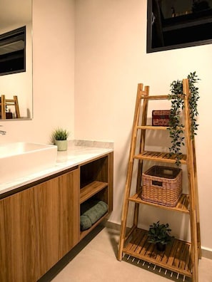 Ein Badezimmer mit einem Holzkonsolenunterschrank, einem Spiegel, einem Waschbecken und einem Holzregal mit Pflanzen.
