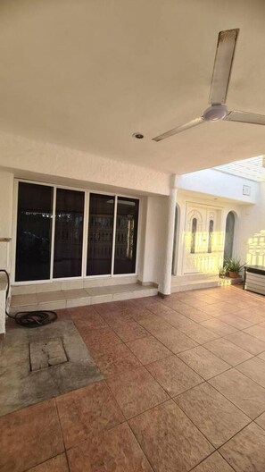 Eine geräumige überdachte Terrasse mit großen Fenstern und einem Deckenventilator.
