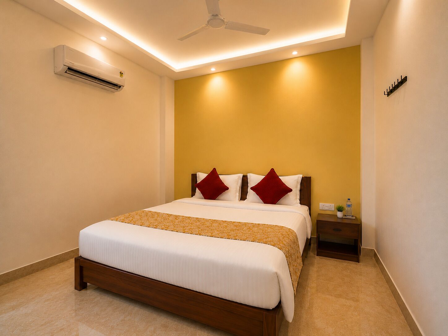 A hotel room with a bed, a nightstand, a wall-mounted air conditioner, and a ceiling fan.