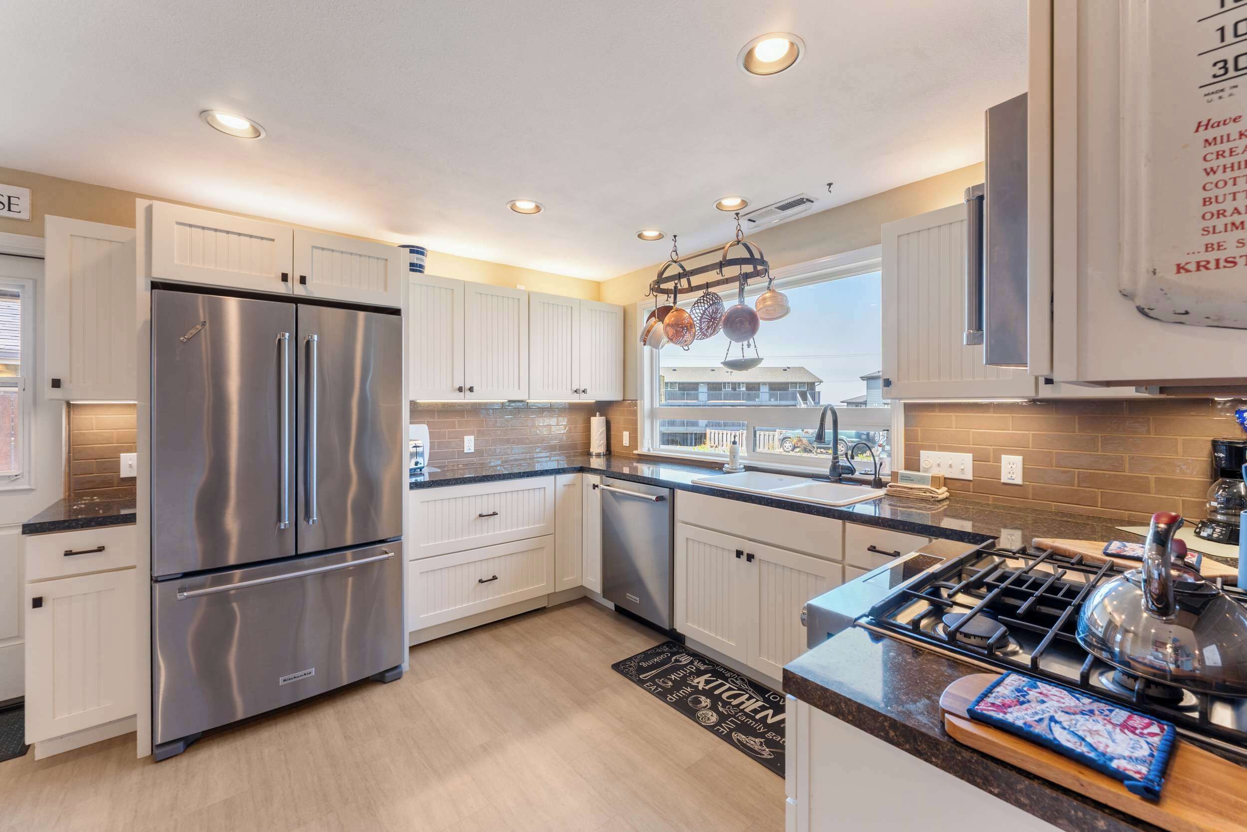A modern kitchen with stainless steel appliances, white cabinetry, and a large window providing a view of the outside.