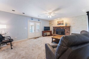 A living room with a fireplace, a ceiling fan, and a television. - Pet-friendly - Walk to the beach, explore downtown Newport, and unwind in this cozy coastal getaway just steps from the Oregon coast (Newport)