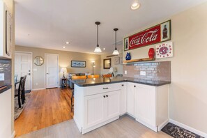 A kitchen with white cabinetry, a central island, and a Coca-Cola sign above the island. - Pet-friendly - Walk to the beach, explore downtown Newport, and unwind in this cozy coastal getaway just steps from the Oregon coast (Newport)