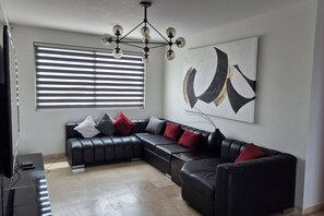 A modern living room with a sectional sofa, a chandelier, a large abstract painting, and a piano. - Depa moderno piso7- Recamaras -Elevador+2 cajones (Zapopan)