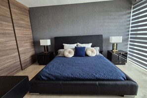 Une chambre à coucher moderne avec un grand lit, deux tables de chevet et une tête de lit sombre.