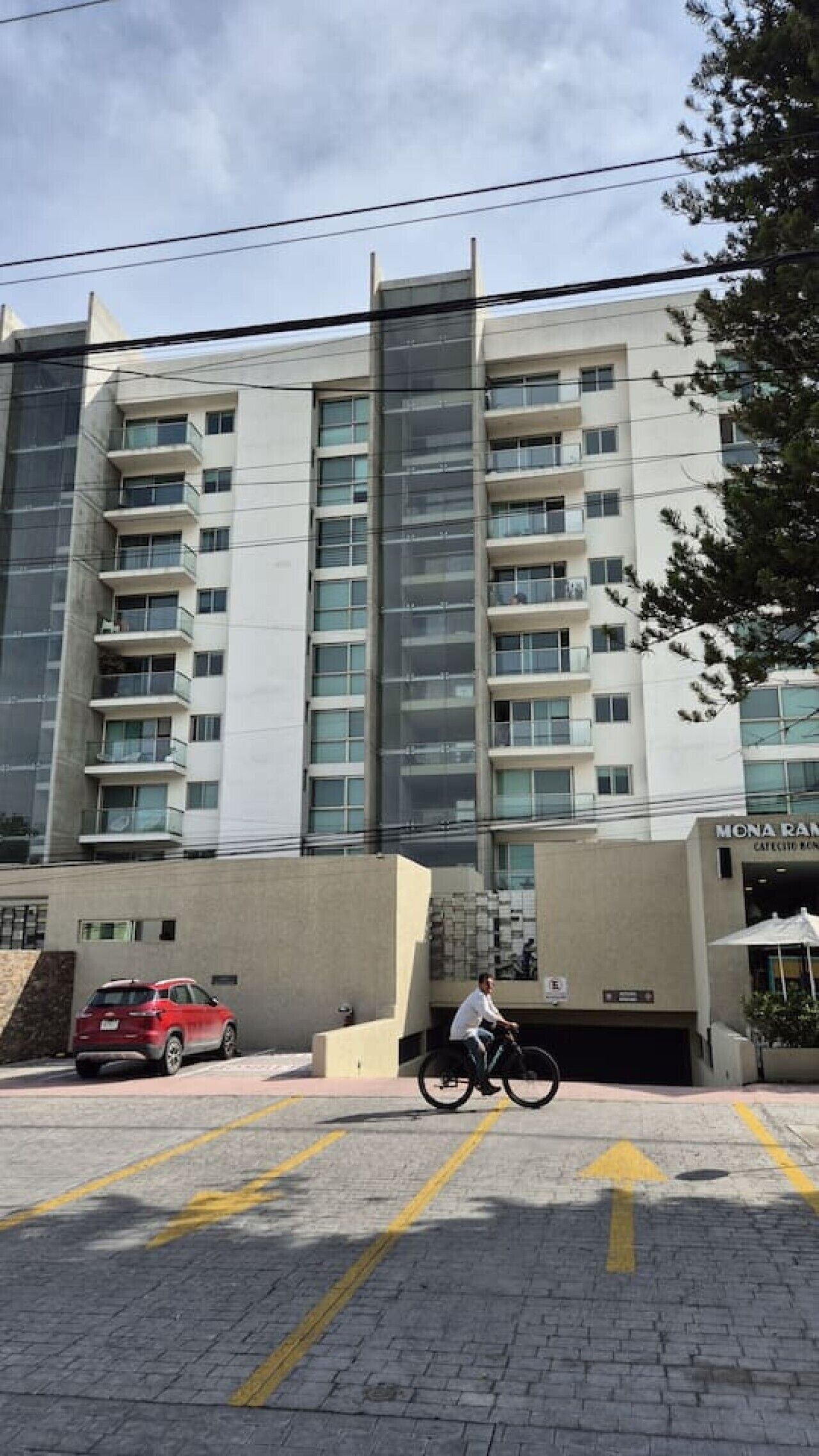 A multi-story building with a parking area and a person riding a bicycle.