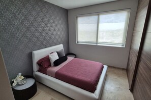 A bedroom with a bed, a window, and a patterned wall. - Depa moderno piso7- Recamaras -Elevador+2 cajones (Zapopan)