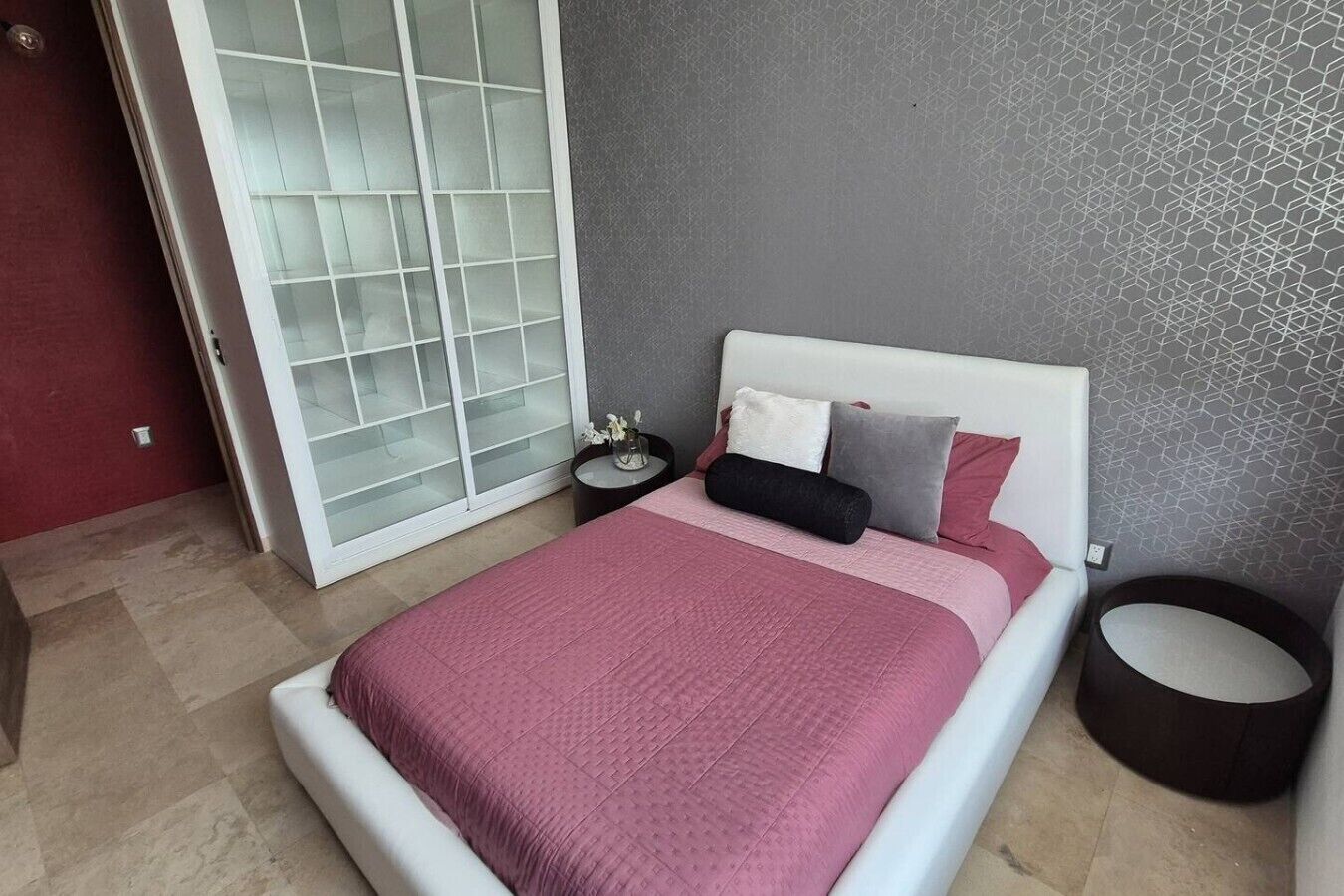 A bedroom with a bed, a nightstand, a round table, and a sliding glass door.