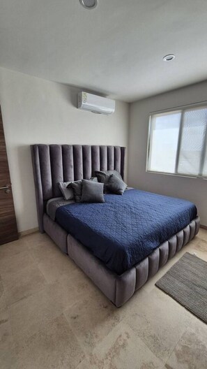 Ein Schlafzimmer mit Bett, Kissen, Kopfteil, einem Fenster und einer Klimaanlage.