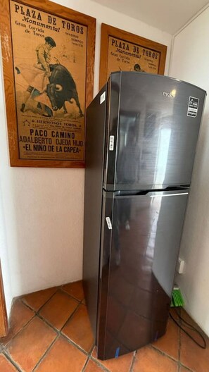 Ein kleiner Kühlschrank in einer Ecke mit gefliestem Boden und zwei Bildern an der Wand.