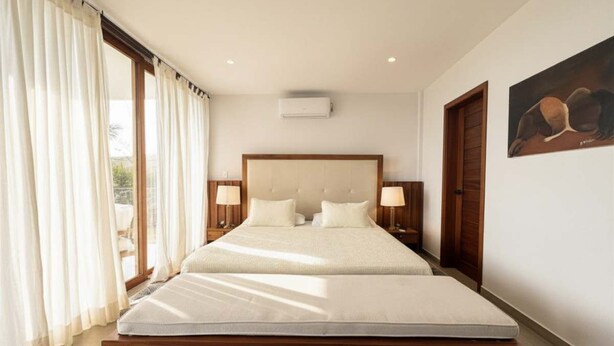 Une chambre d’hôtel avec un grand lit, deux tables de chevet avec des lampes, un climatiseur au plafond et un tableau accroché au mur.