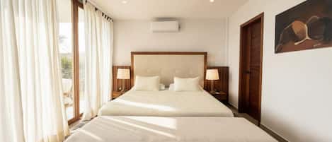 A hotel room with a large bed, two bedside tables with lamps, a ceiling air conditioner, and a painting on the wall.