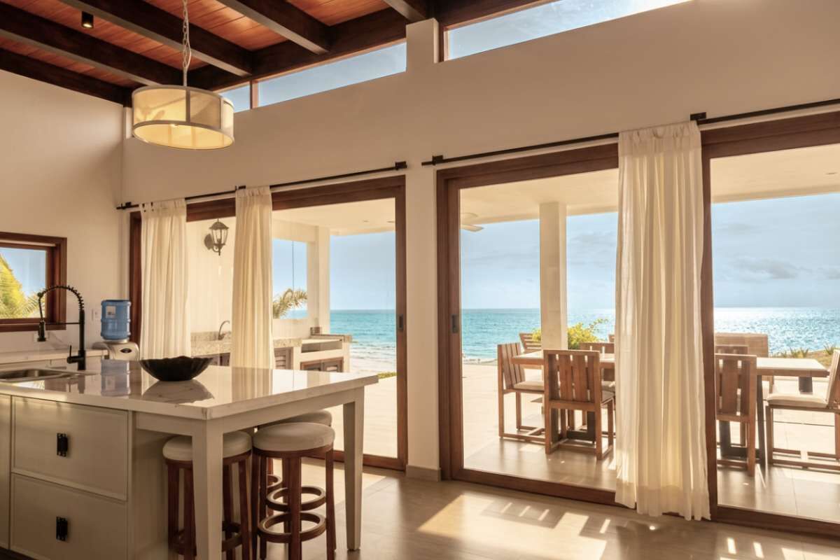 Una cocina con una isla grande, un comedor con sillas de madera y vistas al océano a través de amplios ventanales correderos.