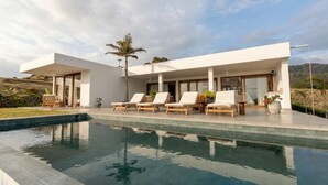 Une maison moderne dotée d’une piscine, de chaises longues et offrant une vue sur le paysage.